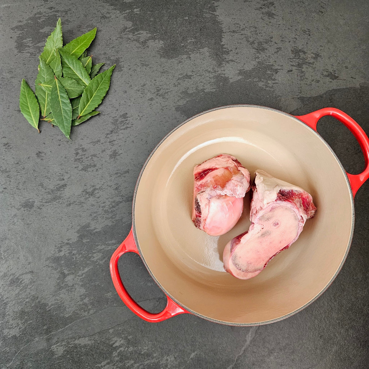 Grass-fed beef femur bone ends in a red Le Creuset Dutch oven with fresh bay leaves — Wishbone Heritage Farms, Saint George, SC