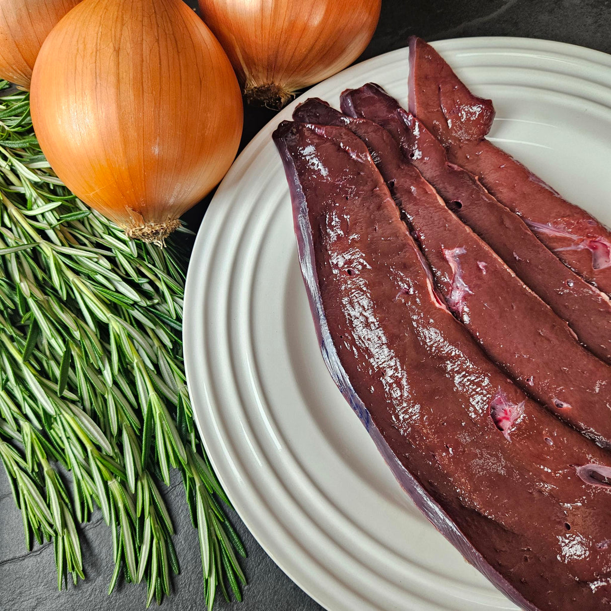 Grass-fed beef liver slices on a white plate with fresh rosemary and yellow onions — Wishbone Heritage Farms, Saint George, SC