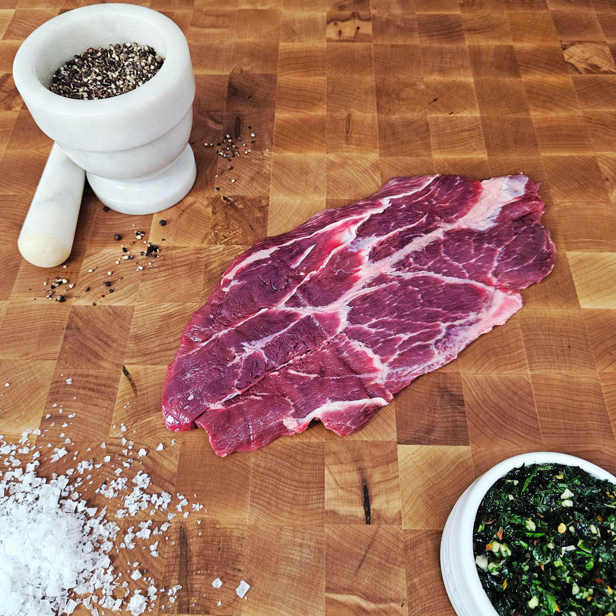 Grass-fed beef sierra steak on an end-grain butcher block with flake salt, cracked pepper, and chimichurri — Wishbone Heritage Farms, Saint George, SC