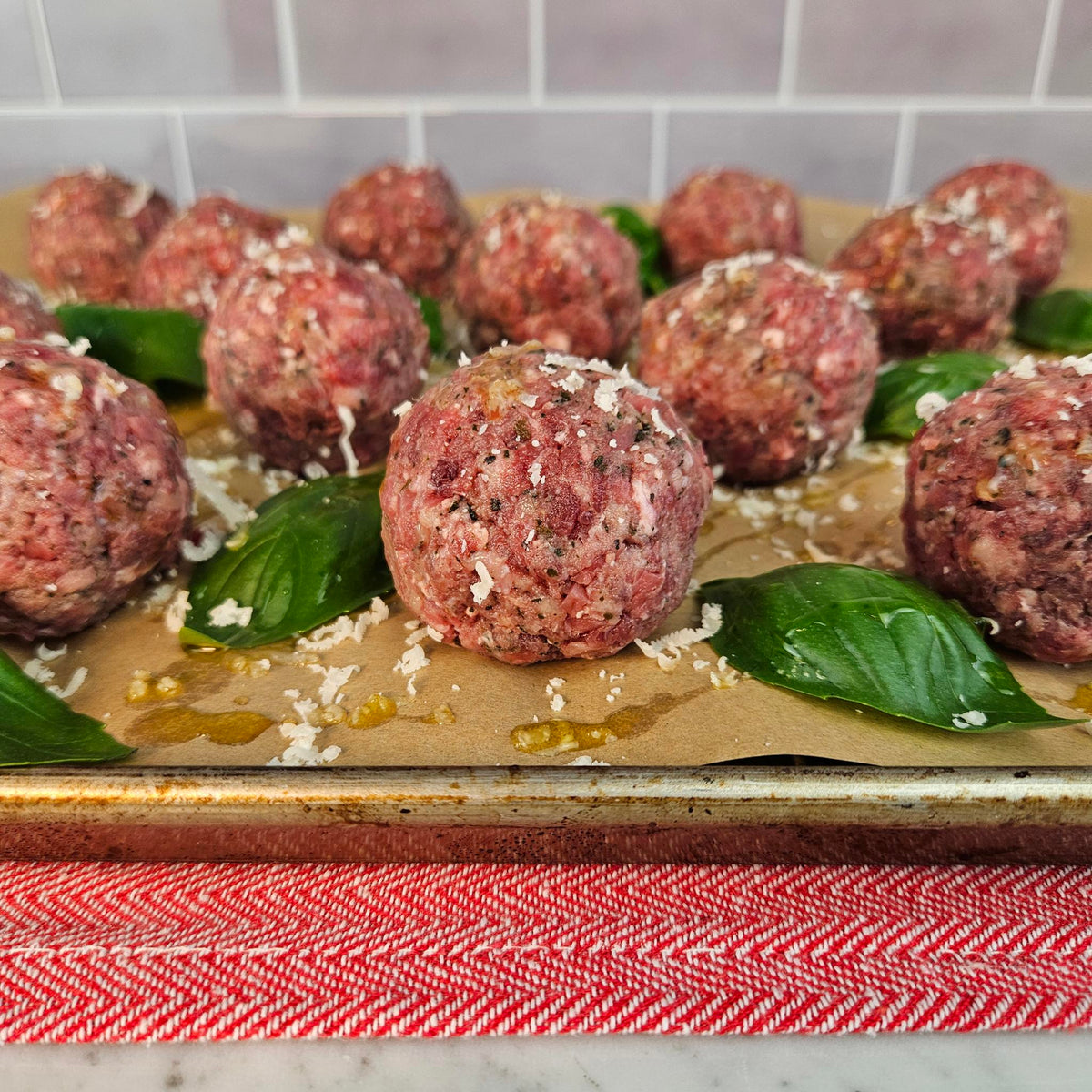Raw grass-fed beef meatballs on a parchment-lined sheet pan with fresh basil, grated Parmesan, and olive oil — Wishbone Heritage Farms, Saint George, SC