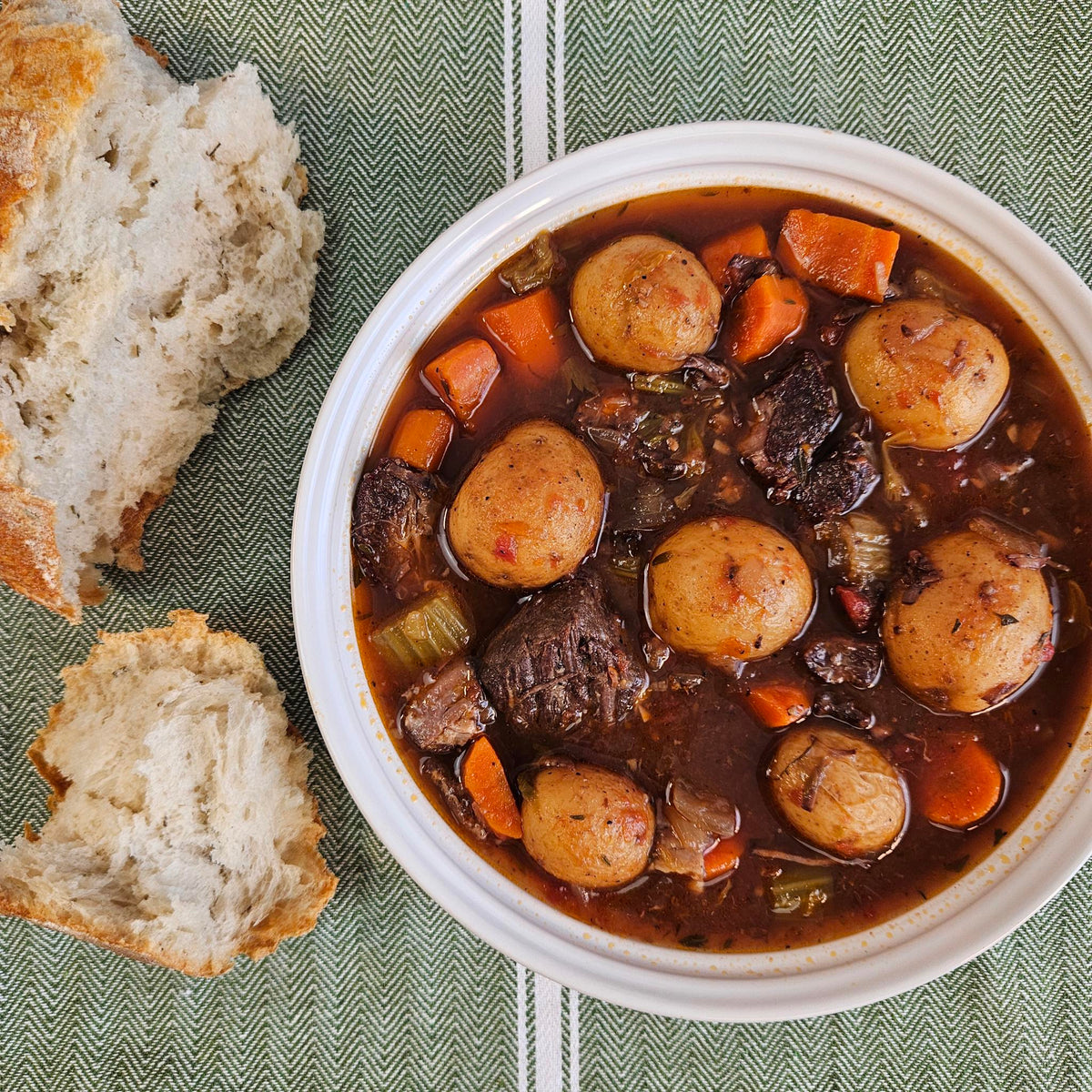 Grass-fed beef stew with tender beef chunks, baby potatoes, carrots, and celery in a rich broth, served in a white bowl with torn crusty bread — Wishbone Heritage Farms, Saint George, SC