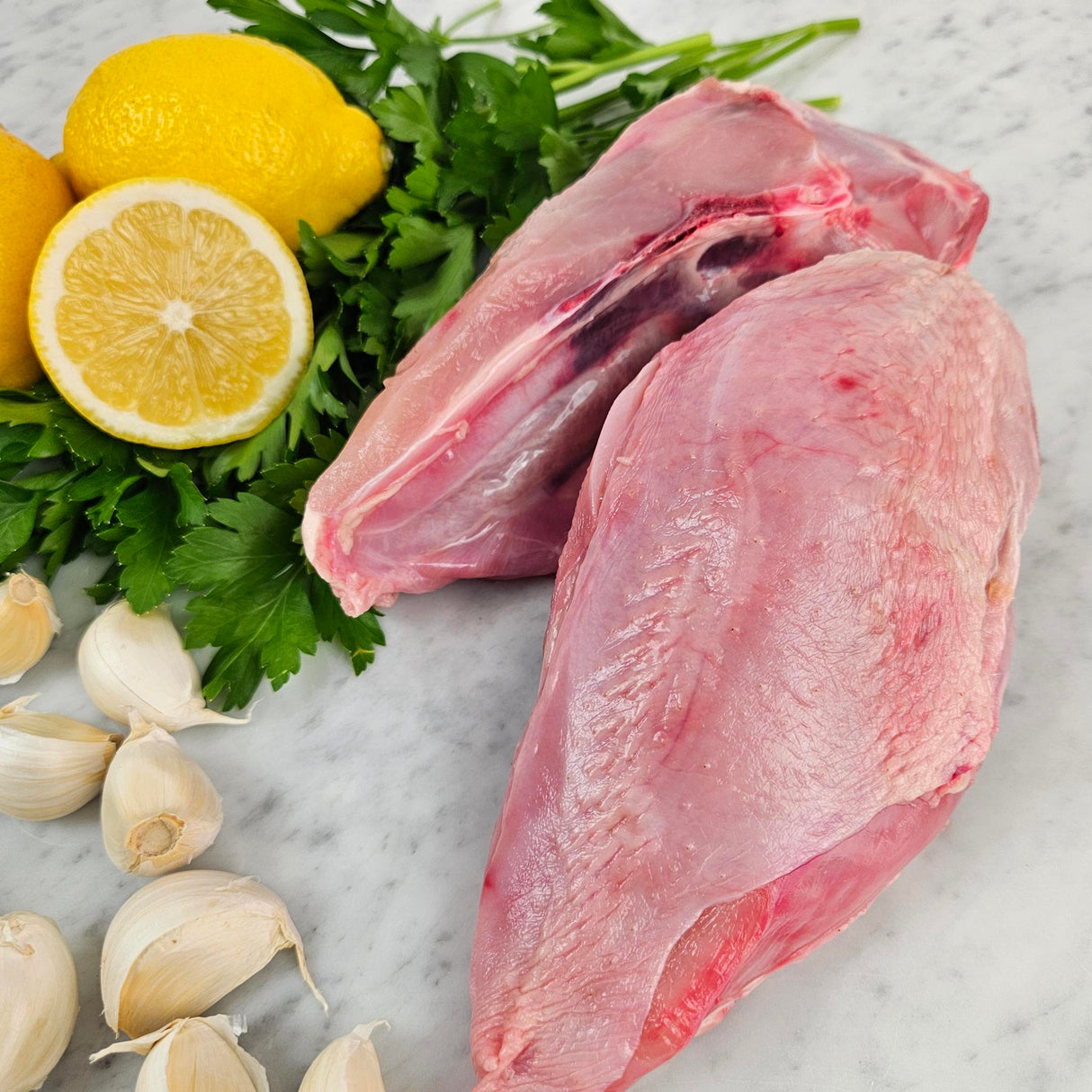 Raw pasture-raised bone-in chicken breasts on white marble with lemon, garlic, and fresh parsley — Wishbone Heritage Farms, South Carolina
