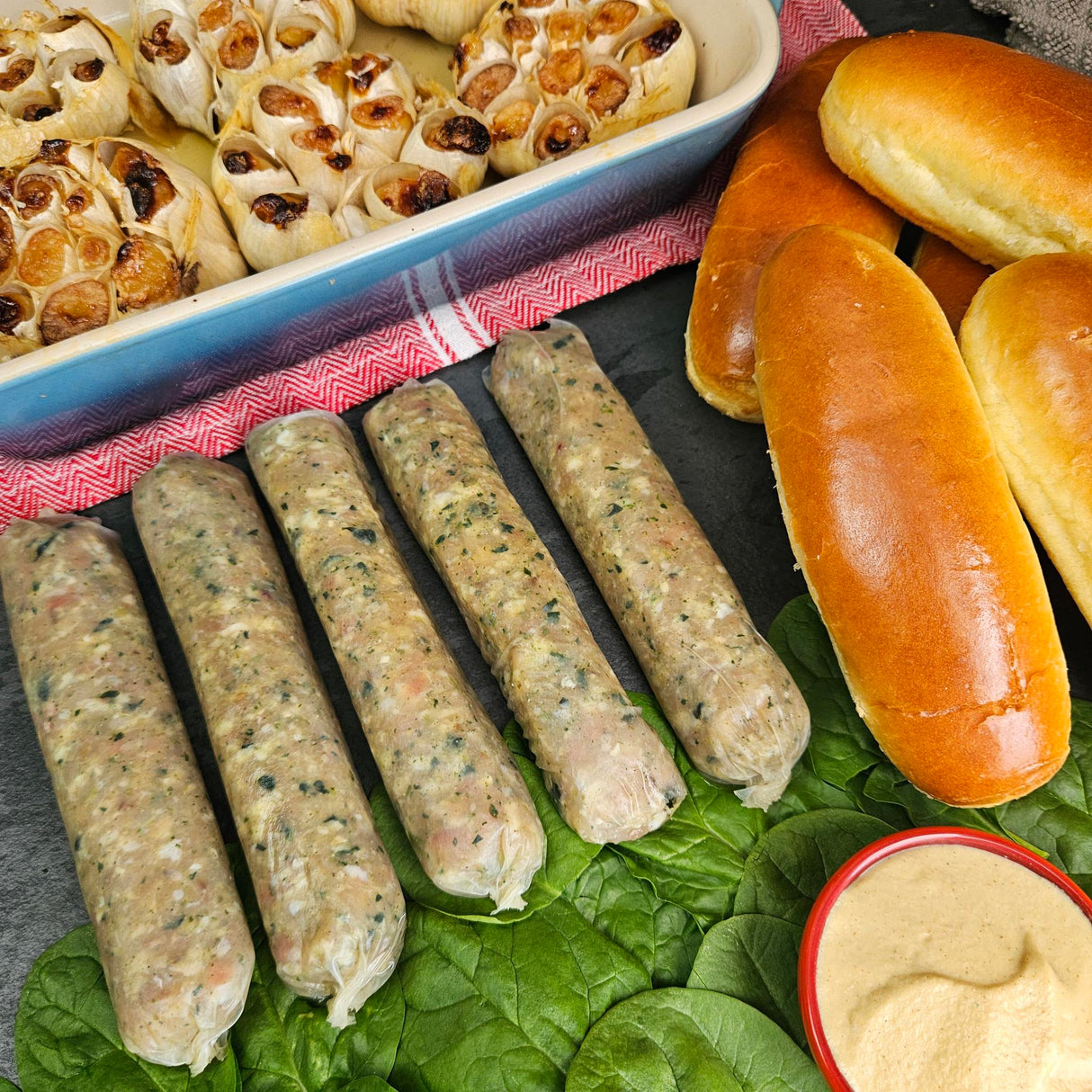 Raw pasture-raised roasted garlic and spinach chicken sausage links on fresh spinach with roasted garlic, brioche buns, and whole grain mustard — Wishbone Heritage Farms, Saint George, SC