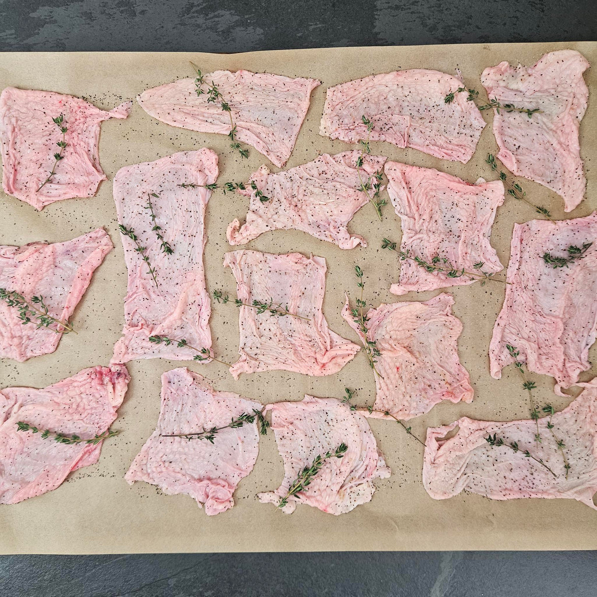 Pasture-raised chicken skins seasoned with black pepper and fresh thyme on a parchment-lined baking sheet — Wishbone Heritage Farms, Saint George, SC