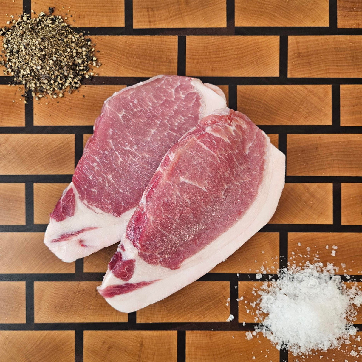Pasture-raised heritage breed boneless center cut pork chops on an end-grain butcher block with flake salt and cracked pepper — Wishbone Heritage Farms, Saint George, SC