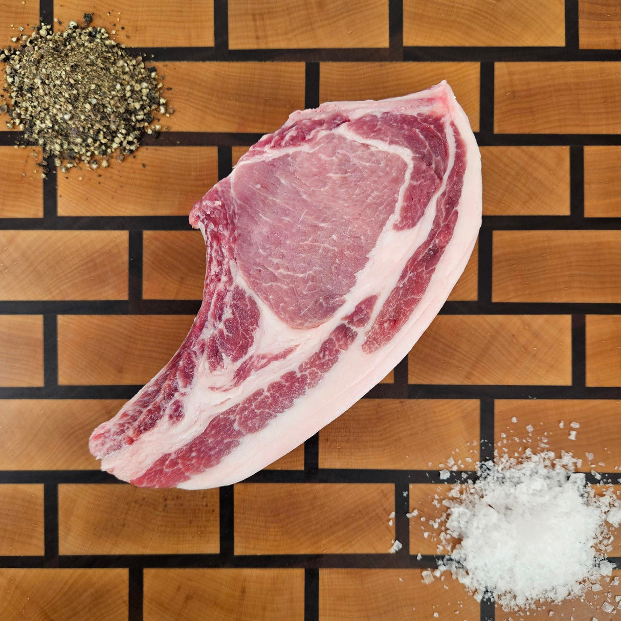 Pasture-raised heritage breed thick-cut center cut pork chop on an end-grain butcher block with flake salt and cracked pepper — Wishbone Heritage Farms, Saint George, SC