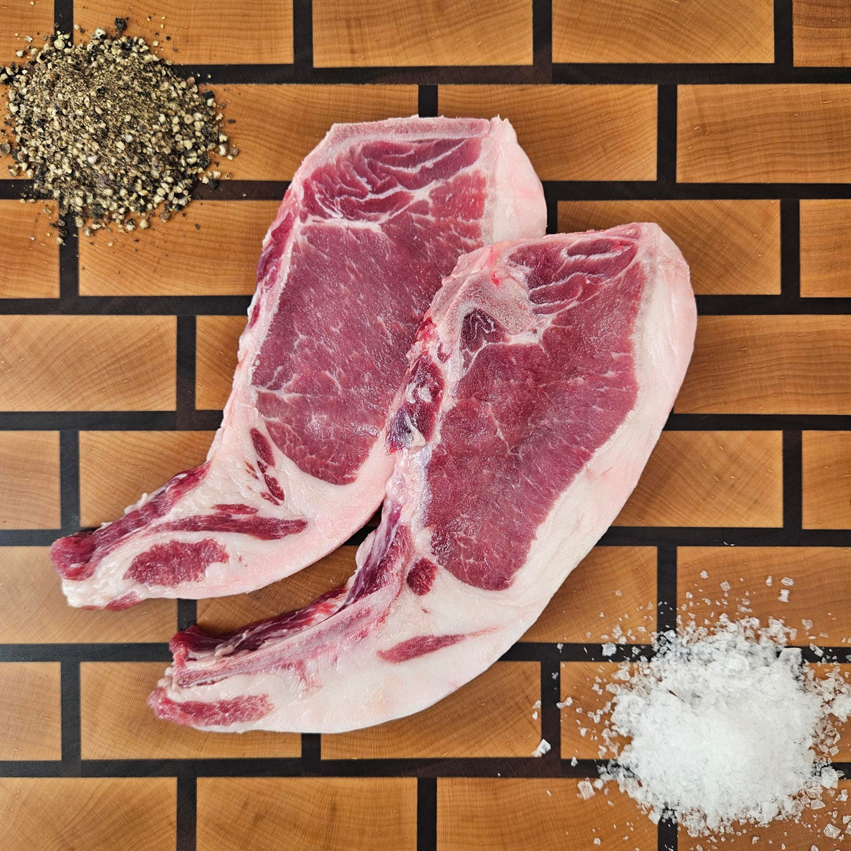 Pasture-raised heritage breed thin center cut bone-in pork chop on an end-grain butcher block with flake salt and cracked pepper — Wishbone Heritage Farms, Saint George, SC