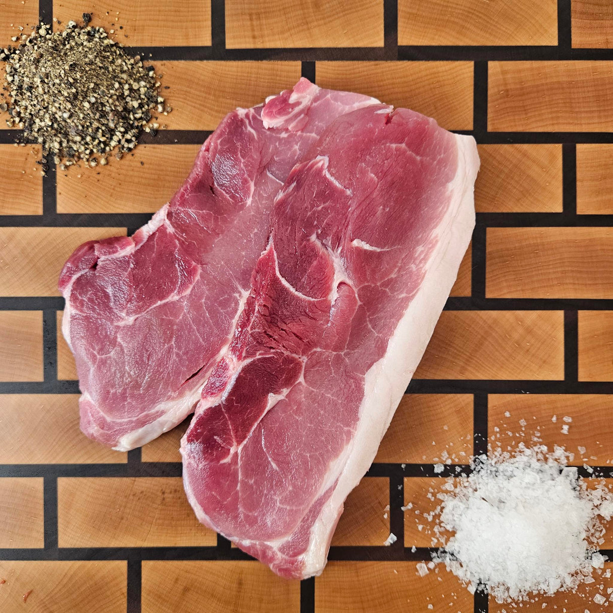Pasture-raised heritage breed sirloin cut pork chop on an end-grain butcher block with flake salt and cracked pepper — Wishbone Heritage Farms, Saint George, SC