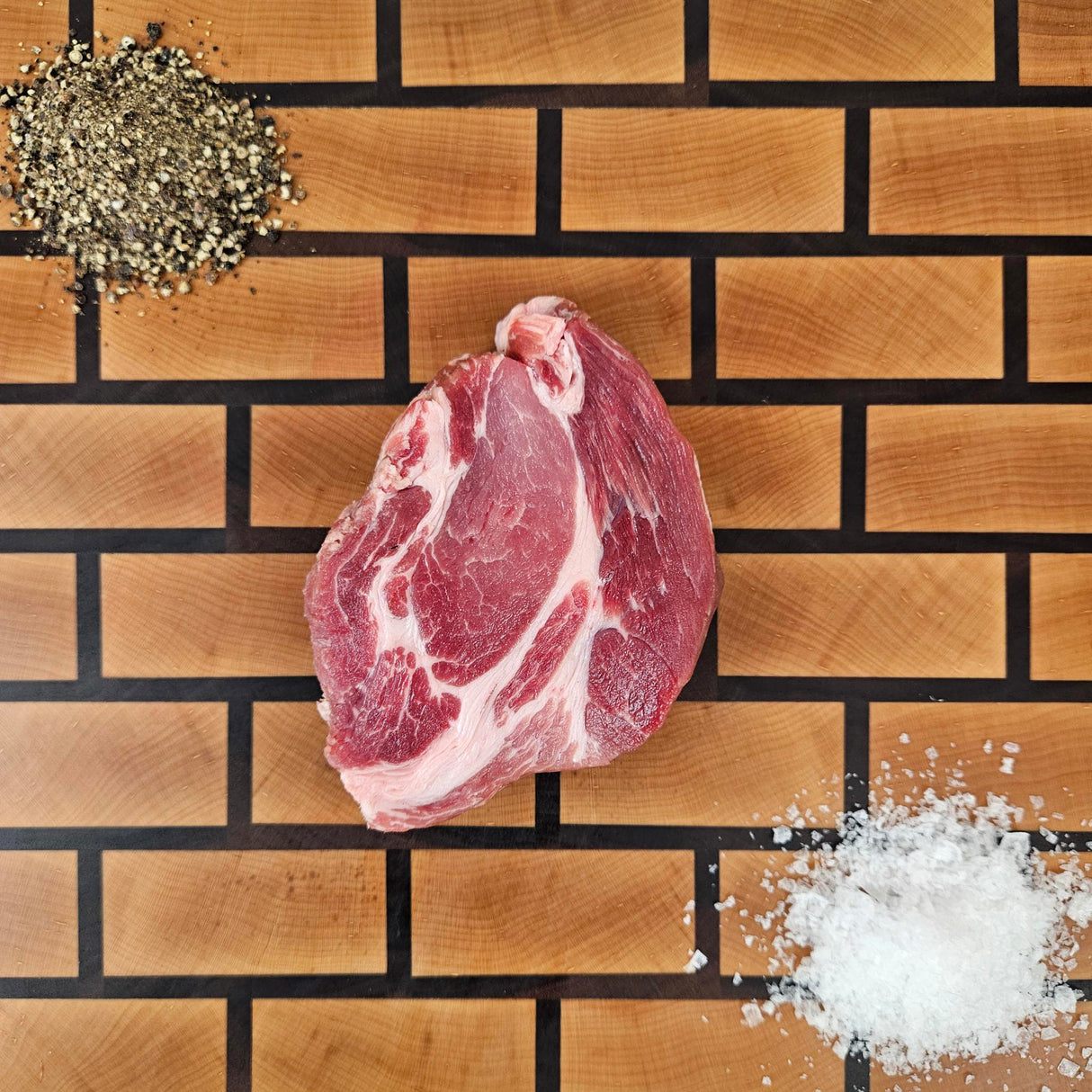Pasture-raised heritage breed pork coppa steak on an end-grain butcher block with flake salt and cracked pepper — Wishbone Heritage Farms, Saint George, SC