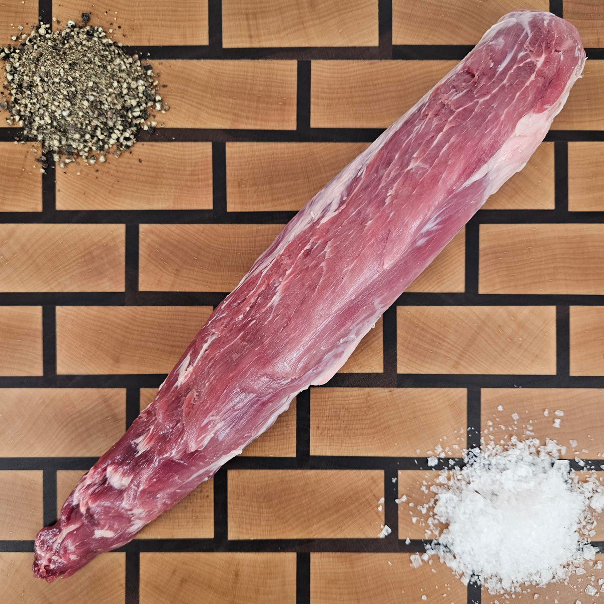 Pasture-raised heritage breed pork tenderloin on an end-grain butcher block with flake salt and cracked pepper — Wishbone Heritage Farms, Saint George, SC