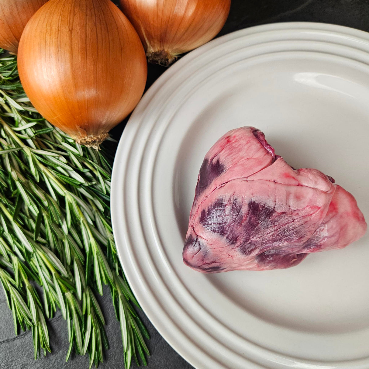 Pasture-raised heritage pork heart on a white plate with fresh rosemary and yellow onions — Wishbone Heritage Farms, Saint George, SC