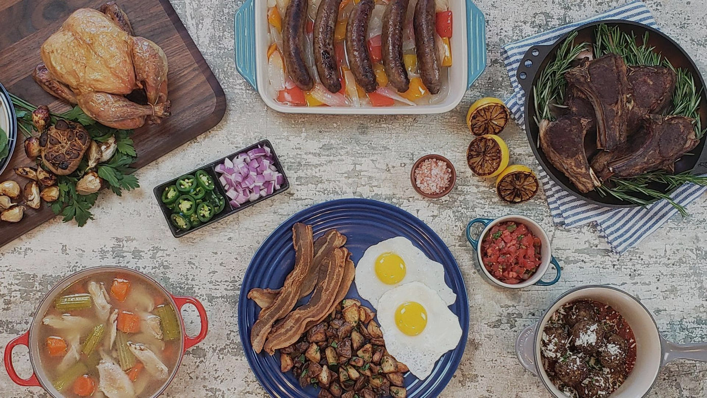 Overhead spread of Wishbone Heritage Farms pasture-raised meals — roasted whole chicken, sausage and peppers, pan-seared steaks, bacon and eggs with breakfast potatoes, chicken soup, and meatballs — Saint George, South Carolina