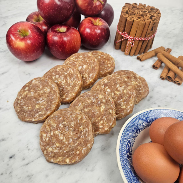 Raw pasture raised apple cinnamon chicken breakfast patties on marble with fresh apples, cinnamon sticks, and eggs