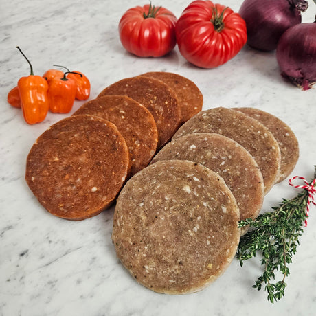Raw pasture raised chicken sandwich patties on marble surface with heirloom tomatoes, red onion, habanero peppers, and fresh thyme
