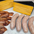 Raw grass-fed beef bacon cheeseburger sausage links on white marble with crispy cooked bacon and a wedge of aged cheddar — Wishbone Heritage Farms, Saint George, SC