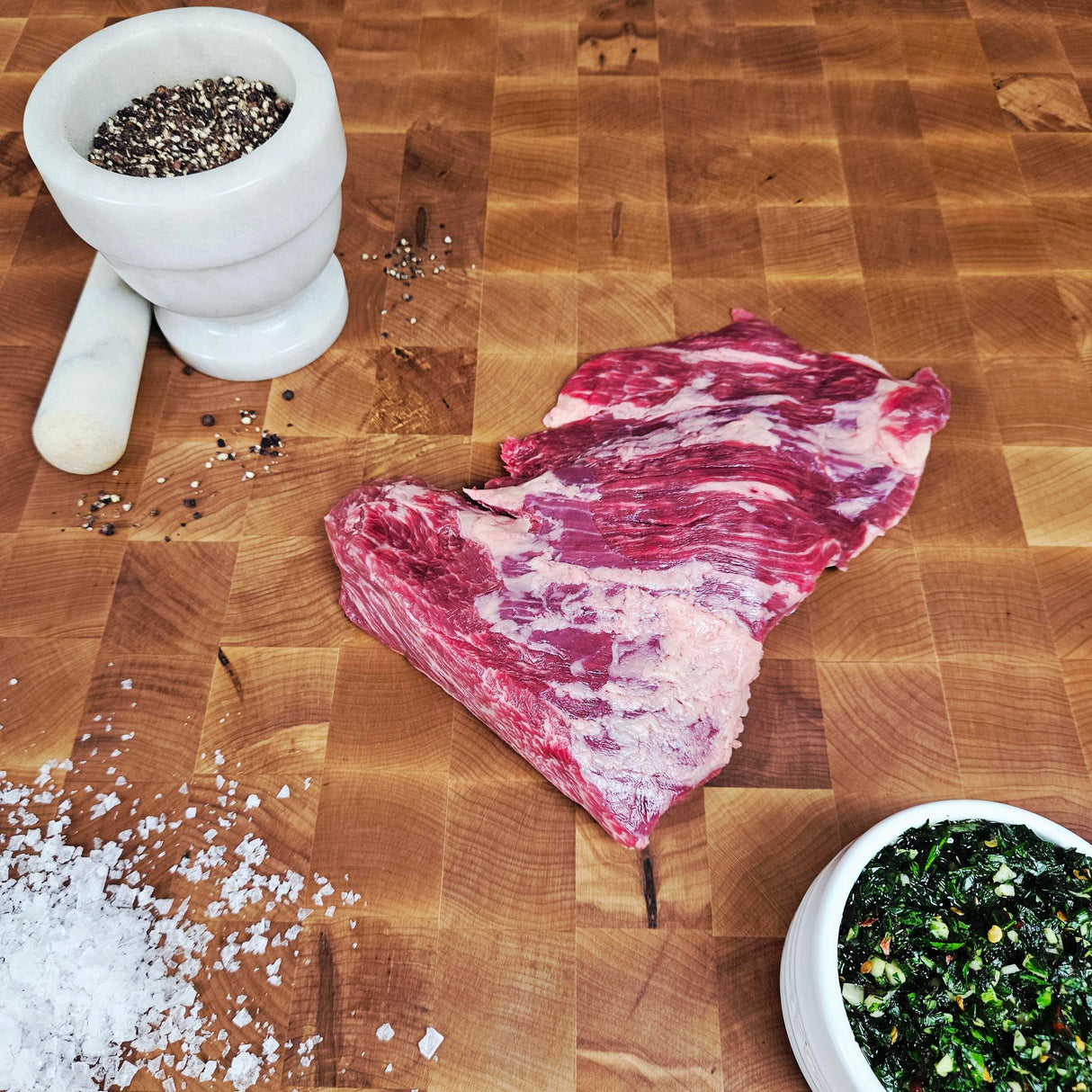 Grass-fed beef bavette steak on an end-grain butcher block with flake salt, cracked pepper, and chimichurri — Wishbone Heritage Farms, Saint George, SC