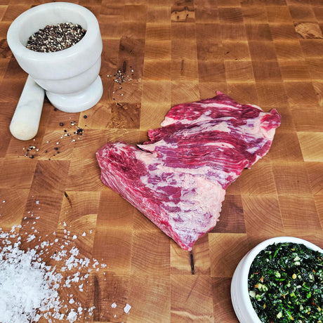Grass-fed beef bavette steak on an end-grain butcher block with flake salt, cracked pepper, and chimichurri — Wishbone Heritage Farms, Saint George, SC