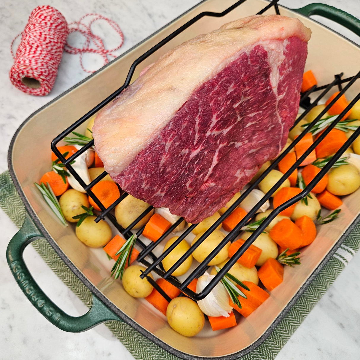 Grass-fed beef bottom round roast in a green Le Creuset roasting pan with potatoes, carrots, garlic, rosemary, and butcher's twine — Wishbone Heritage Farms, Saint George, SC