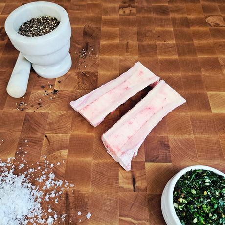 Grass-fed beef canoe cut marrow bones on an end-grain butcher block with flake salt, cracked pepper, and chimichurri — Wishbone Heritage Farms, Saint George, SC