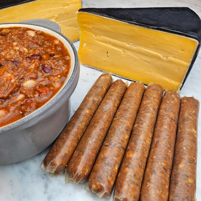 Raw grass-fed beef chili cheese dogs on white marble with a pot of beef chili and a wedge of aged cheddar — Wishbone Heritage Farms, Saint George, SC