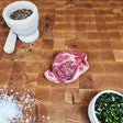 Grass-fed beef Delmonico steak on an end-grain butcher block with flake salt, cracked pepper, and chimichurri — Wishbone Heritage Farms, Saint George, SC