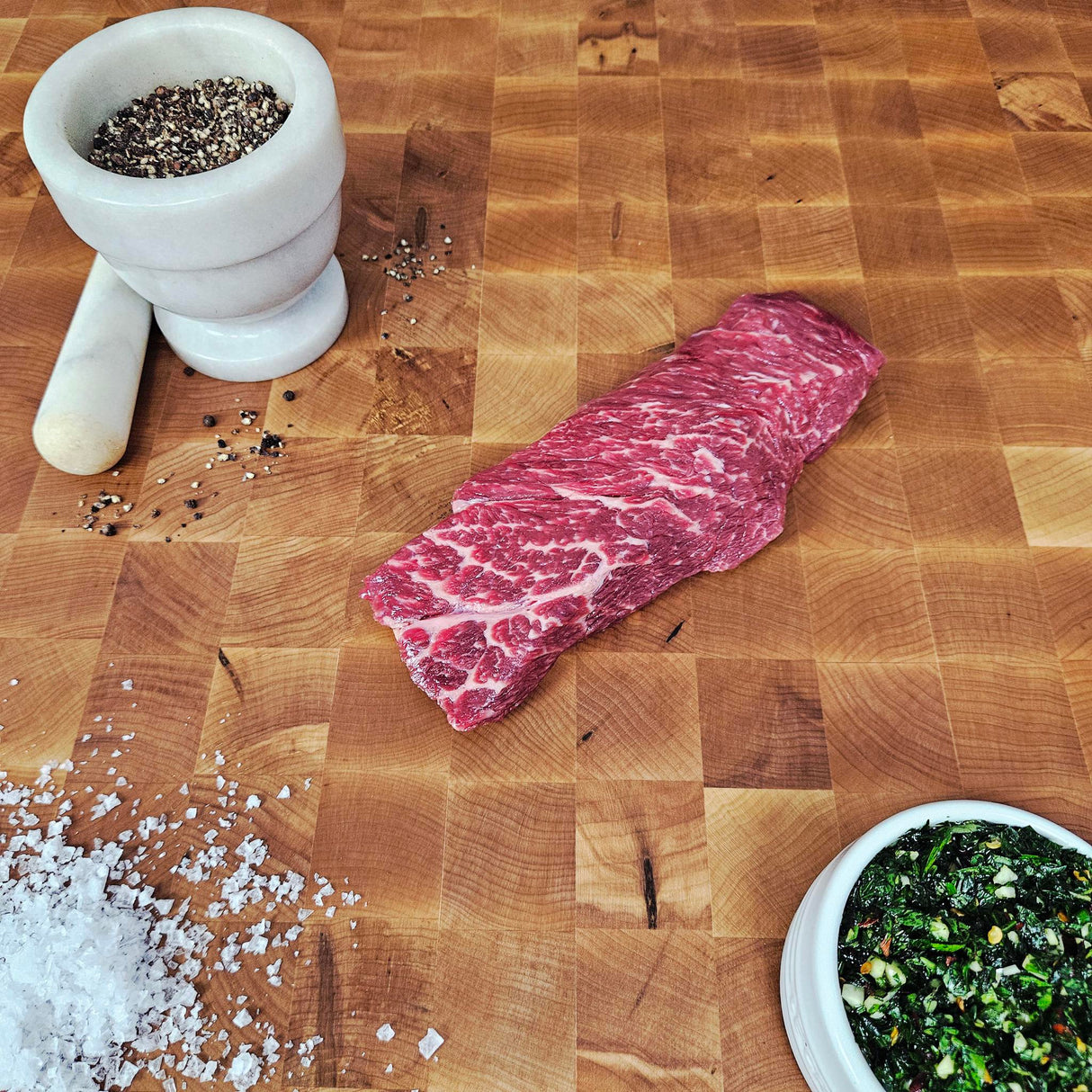Grass-fed beef Denver steak on an end-grain butcher block with flake salt, cracked pepper, and chimichurri — Wishbone Heritage Farms, Saint George, SC