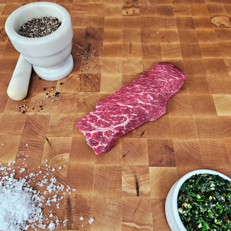 Grass-fed beef Denver steak on an end-grain butcher block with flake salt, cracked pepper, and chimichurri — Wishbone Heritage Farms, Saint George, SC