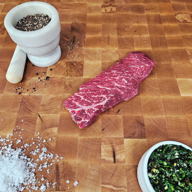 Grass-fed beef Denver steak on an end-grain butcher block with flake salt, cracked pepper, and chimichurri — Wishbone Heritage Farms, Saint George, SC