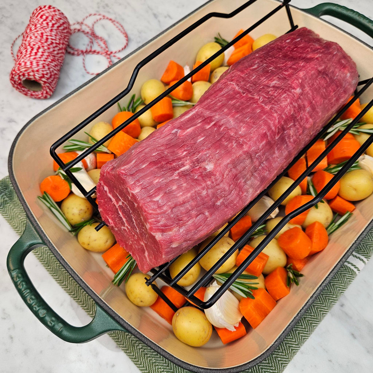 Grass-fed beef eye round roast in a green Le Creuset roasting pan with potatoes, carrots, garlic, rosemary, and butcher's twine — Wishbone Heritage Farms, Saint George, SC