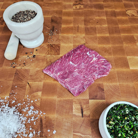Grass-fed beef flat iron steak on an end-grain butcher block with flake salt, cracked pepper, and chimichurri — Wishbone Heritage Farms, Saint George, SC