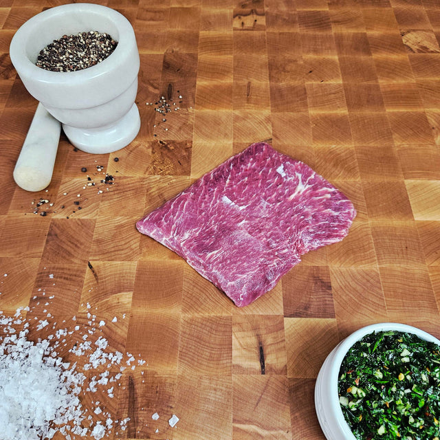 Grass-fed beef flat iron steak on an end-grain butcher block with flake salt, cracked pepper, and chimichurri — Wishbone Heritage Farms, Saint George, SC