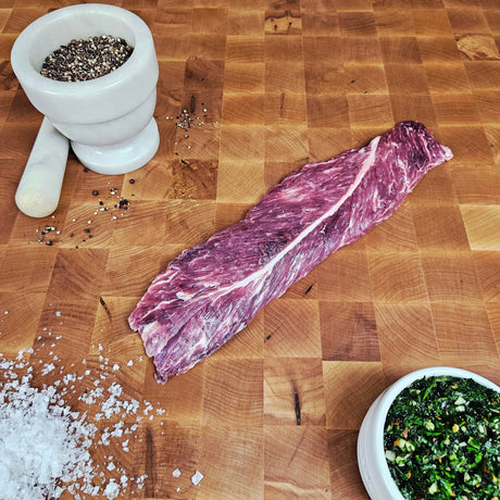 Grass-fed beef hanger steak on an end-grain butcher block with flake salt, cracked pepper, and chimichurri — Wishbone Heritage Farms, Saint George, SC