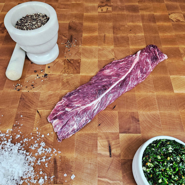 Grass-fed beef hanger steak on an end-grain butcher block with flake salt, cracked pepper, and chimichurri — Wishbone Heritage Farms, Saint George, SC