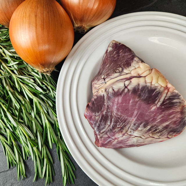 Grass-fed beef heart on a white plate with fresh rosemary and yellow onions — Wishbone Heritage Farms, Saint George, SC