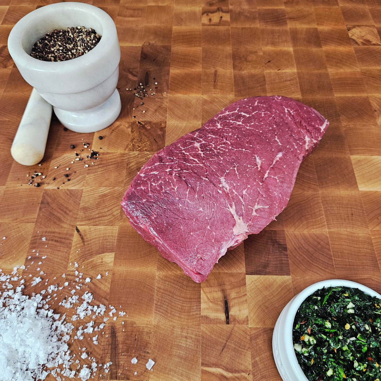 Grass-fed beef london broil on an end-grain butcher block with flake salt, cracked pepper, and chimichurri — Wishbone Heritage Farms, Saint George, SC