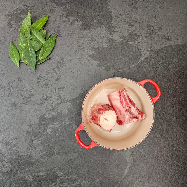 Grass-fed beef cross-cut marrow bones in a red Le Creuset Dutch oven with fresh bay leaves — Wishbone Heritage Farms, Saint George, SC
