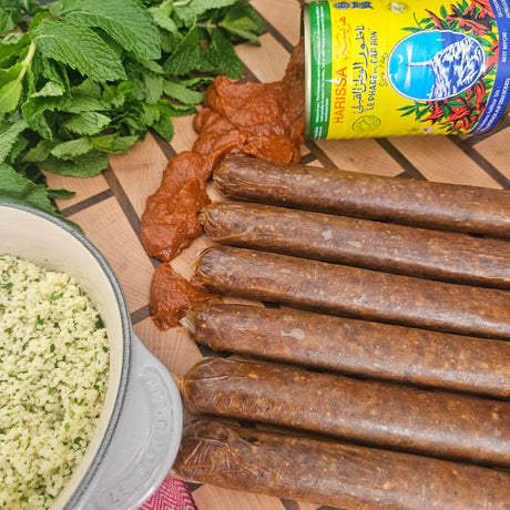 Raw grass-fed beef merguez sausage links on a wooden board with harissa, herbed couscous, and fresh mint — Wishbone Heritage Farms, Saint George, SC