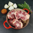 Raw grass fed beef oxtail in red Dutch oven with quartered onion, fresh herbs, and spices