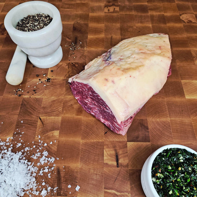 Grass-fed beef picanha on an end-grain butcher block with flake salt, cracked pepper, and chimichurri — Wishbone Heritage Farms, Saint George, SC