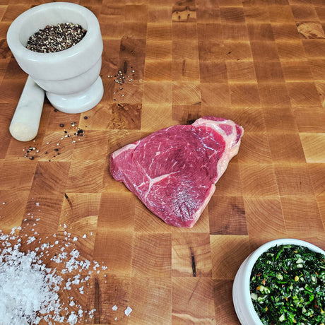 Grass-fed beef sirloin steak on an end-grain butcher block with flake salt, cracked pepper, and chimichurri — Wishbone Heritage Farms, Saint George, SC