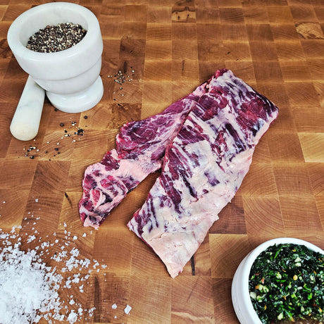 Grass-fed beef skirt steak on an end-grain butcher block with flake salt, cracked pepper, and chimichurri — Wishbone Heritage Farms, Saint George, SC