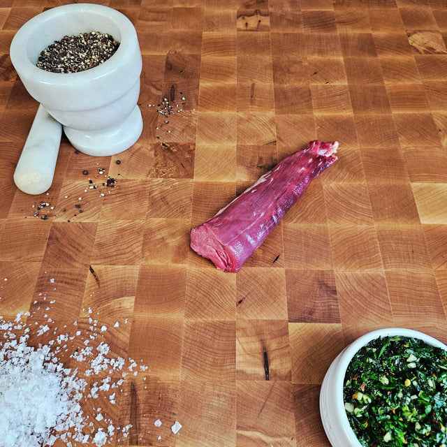 Grass-fed beef tenderloin tail steak on an end-grain butcher block with flake salt, cracked pepper, and chimichurri — Wishbone Heritage Farms, Saint George, SC