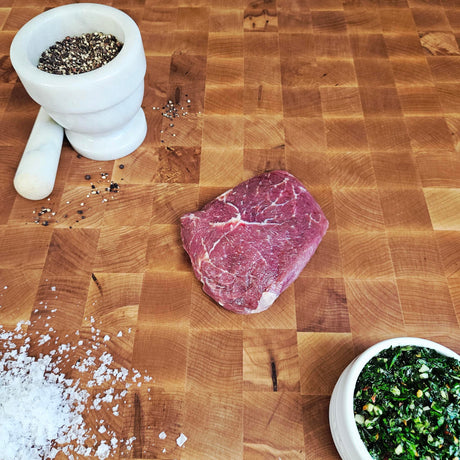 Grass-fed beef top sirloin filet steak on an end-grain butcher block with flake salt, cracked pepper, and chimichurri — Wishbone Heritage Farms, Saint George, SC