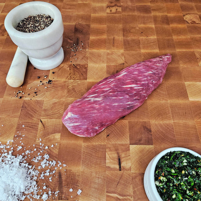 Grass-fed beef tri-tip on an end-grain butcher block with flake salt, cracked pepper, and chimichurri — Wishbone Heritage Farms, Saint George, SC