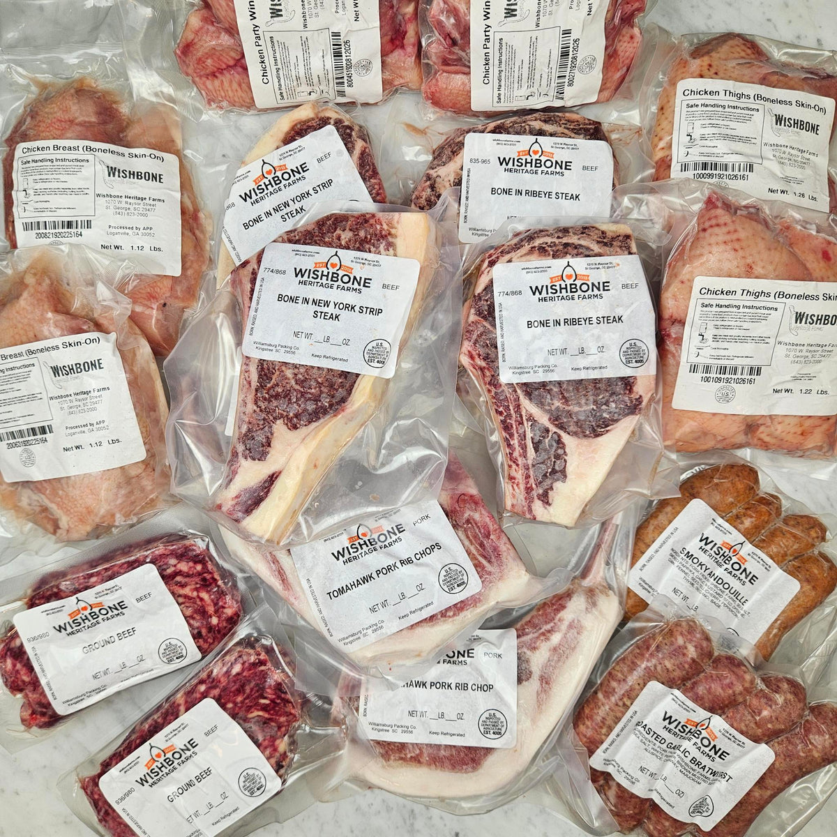 Wishbone Heritage Farms Grill Master's Dream Bundle — bone-in NY strip steaks, bone-in ribeye steaks, tomahawk pork rib chops, chicken wings, boneless skin-on chicken breasts, boneless skin-on chicken thighs, ground beef, smoky andouille, and roasted garlic bratwurst in vacuum-sealed packaging — Saint George, SC