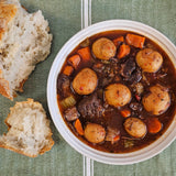 Grass-fed beef stew with tender beef chunks, baby potatoes, carrots, and celery in a rich broth, served in a white bowl with torn crusty bread — Wishbone Heritage Farms, Saint George, SC