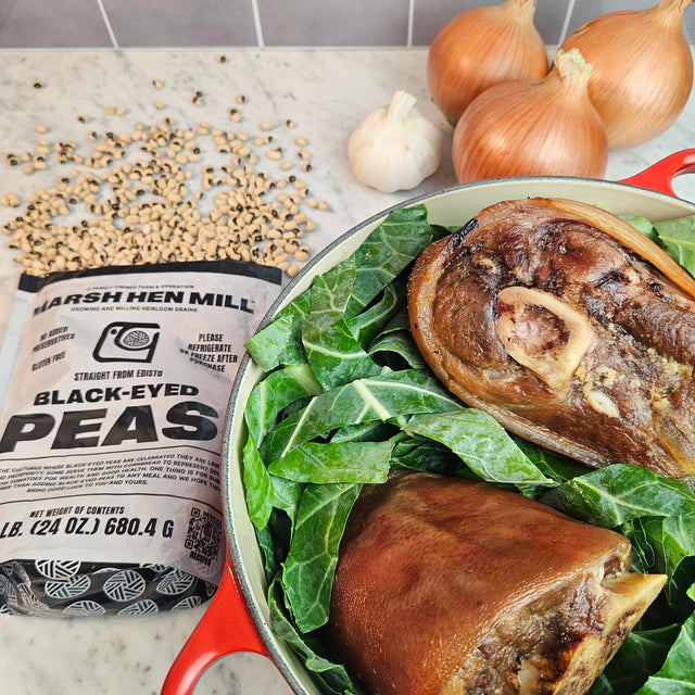 Pasture-raised heritage pork smoked ham hocks on collard greens in a red Dutch oven with Marsh Hen Mill black-eyed peas, onions, and garlic — Wishbone Heritage Farms, Saint George, SC