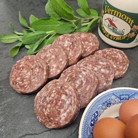 Raw pasture raised maple pork breakfast sausage patties on slate with Vermont maple syrup, fresh sage, and eggs