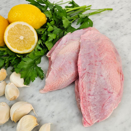 Raw pasture-raised boneless skin-on chicken breasts on white marble with lemon, garlic, and fresh parsley — Wishbone Heritage Farms, South Carolina