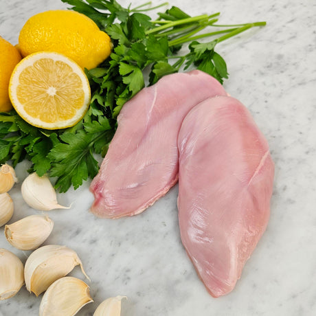 Raw pasture-raised boneless skinless chicken breasts on white marble with lemon, garlic, and fresh parsley — Wishbone Heritage Farms, South Carolina